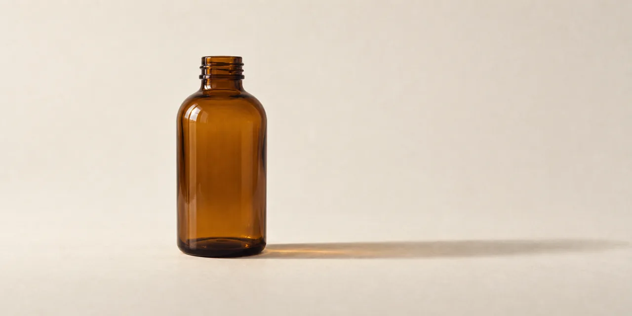 Flacon de verre ambré sans étiquette, debout sur un fond papier clair, ombre portée douce